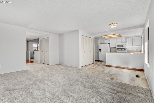 unfurnished living room with light carpet, a textured ceiling, and a sink