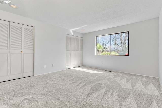 unfurnished bedroom with multiple closets, visible vents, carpet floors, and a textured ceiling