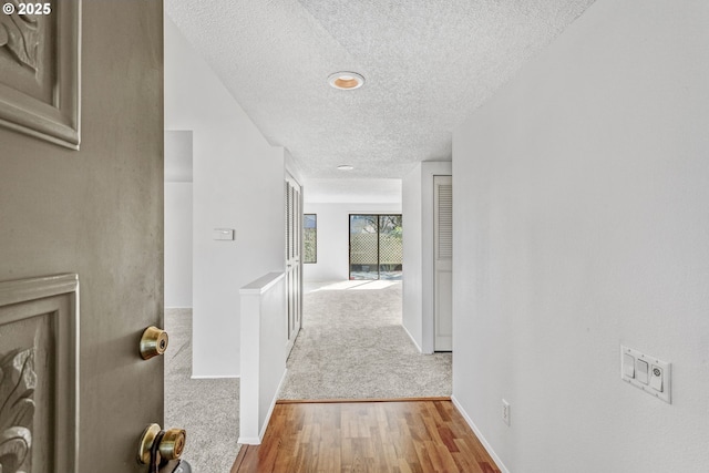 corridor featuring a textured ceiling, baseboards, and wood finished floors