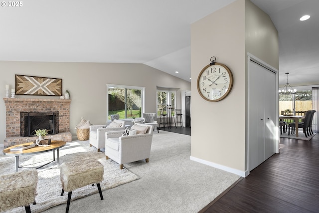 living room with a brick fireplace, baseboards, vaulted ceiling, wood finished floors, and a notable chandelier