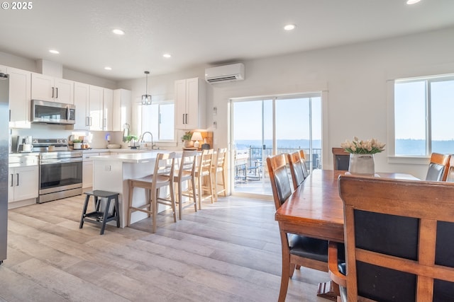 kitchen featuring hanging light fixtures, a wall unit AC, stainless steel appliances, and white cabinets