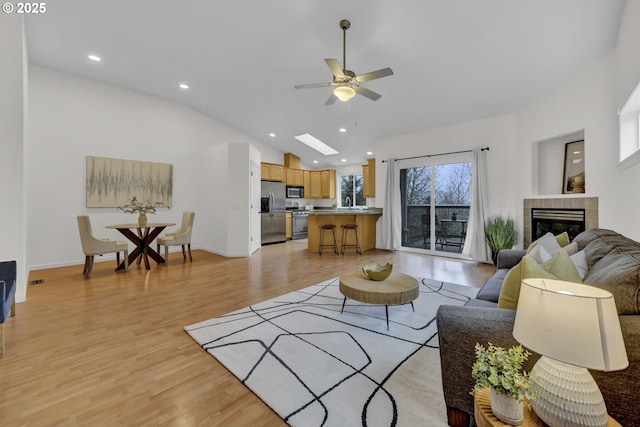 living room with ceiling fan, a tile fireplace, vaulted ceiling, and light hardwood / wood-style floors