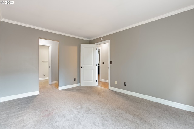 empty room featuring light colored carpet, crown molding, and baseboards