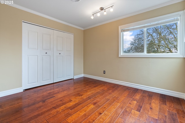 unfurnished bedroom with a closet, baseboards, ornamental molding, and hardwood / wood-style flooring