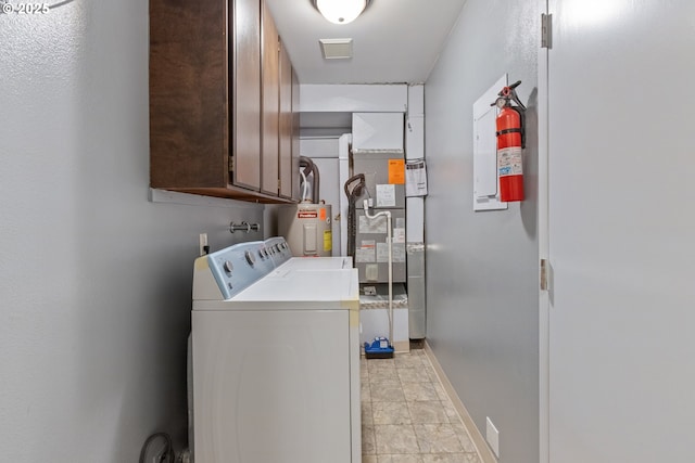 washroom with washing machine and clothes dryer, visible vents, electric water heater, baseboards, and cabinet space