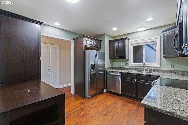 kitchen with a sink, dark wood finished floors, recessed lighting, stainless steel appliances, and light stone countertops