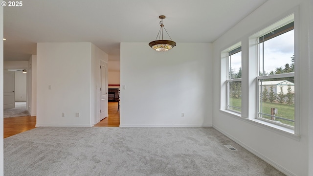 spare room with a ceiling fan, light colored carpet, visible vents, and baseboards