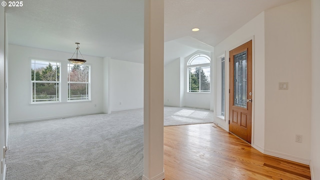 foyer with baseboards, light carpet, a textured ceiling, and vaulted ceiling