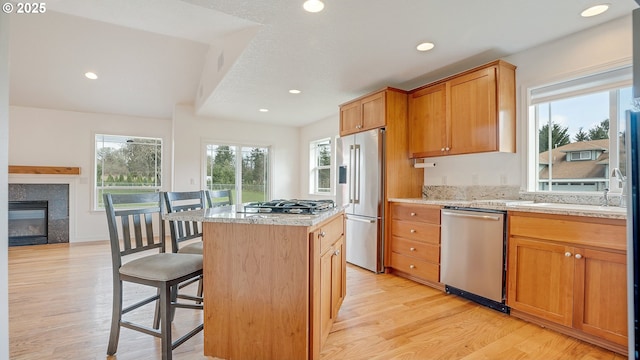 kitchen with light wood-type flooring, a kitchen breakfast bar, a center island, recessed lighting, and appliances with stainless steel finishes