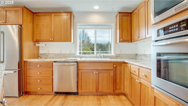 kitchen with recessed lighting, appliances with stainless steel finishes, light wood-style floors, brown cabinetry, and a sink