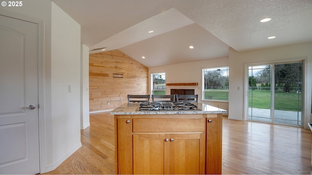 kitchen with a center island, light wood-style floors, stainless steel gas stovetop, wooden walls, and vaulted ceiling