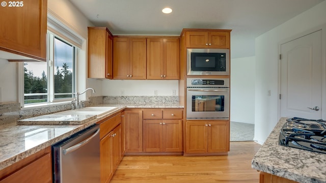 kitchen with a sink, brown cabinets, light wood-type flooring, and stainless steel appliances