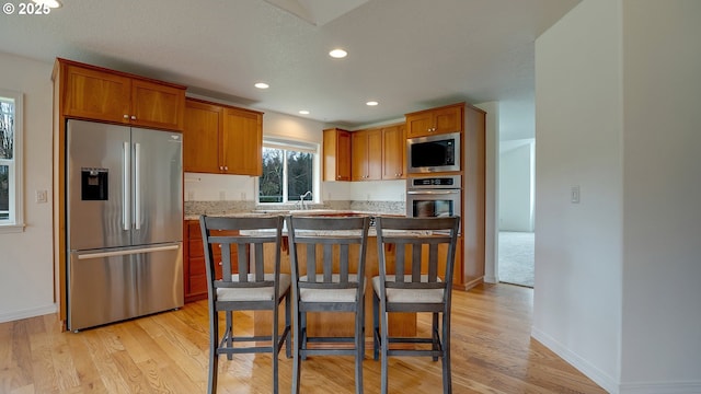 kitchen with light wood-style flooring, appliances with stainless steel finishes, brown cabinets, and a sink