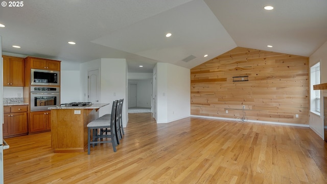 kitchen featuring a kitchen bar, brown cabinets, light wood-style flooring, stainless steel appliances, and wooden walls