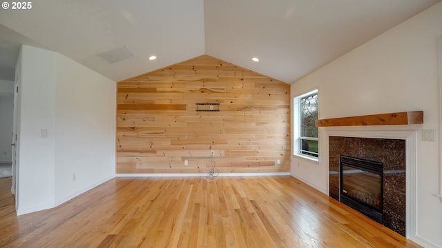 unfurnished living room with wooden walls, visible vents, vaulted ceiling, a tile fireplace, and wood finished floors