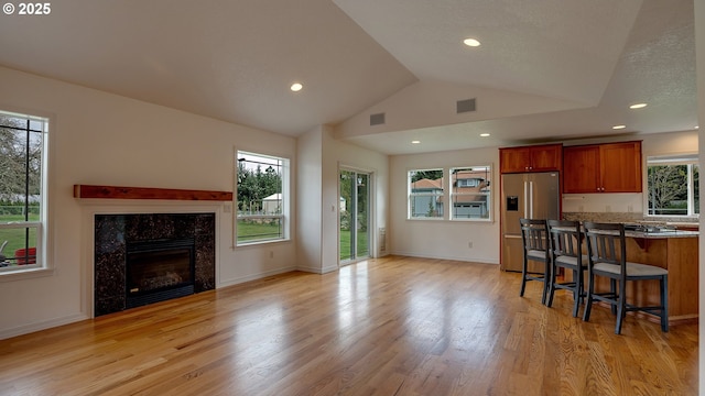 kitchen with a breakfast bar area, light wood finished floors, lofted ceiling, stainless steel fridge, and open floor plan