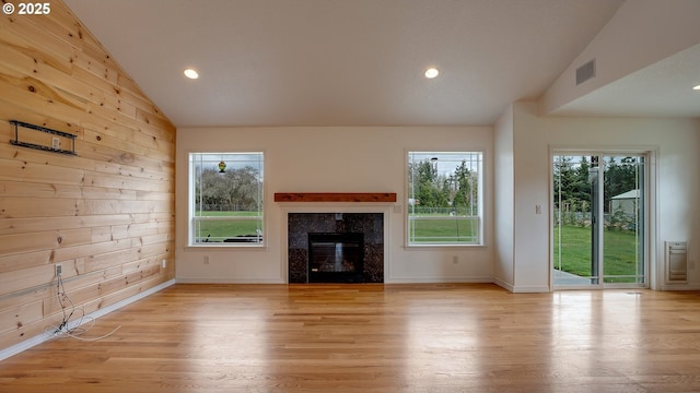 unfurnished living room with light wood-type flooring, wooden walls, visible vents, and vaulted ceiling