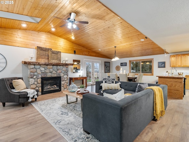 living room featuring lofted ceiling with skylight, ceiling fan, light wood-type flooring, a fireplace, and wood ceiling