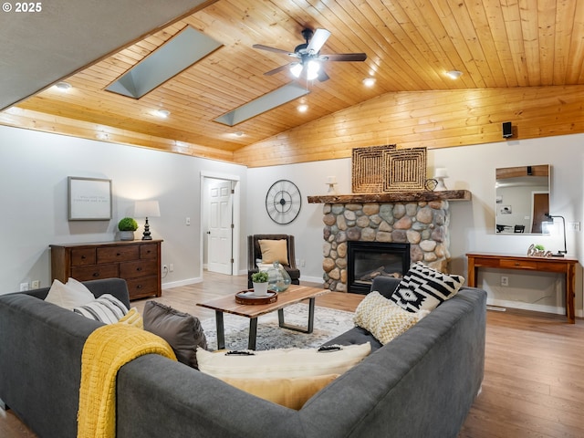 living room with light hardwood / wood-style floors, a stone fireplace, ceiling fan, and wood ceiling