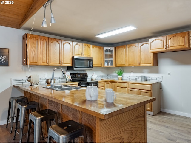 kitchen with kitchen peninsula, sink, light hardwood / wood-style floors, black range with electric stovetop, and a breakfast bar area