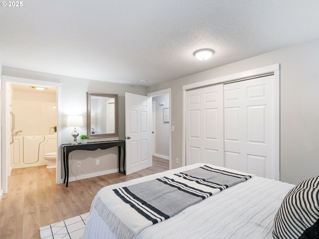 bedroom with ensuite bath, a closet, a textured ceiling, and light wood-type flooring