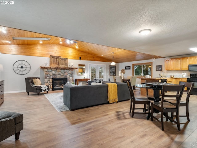 dining space featuring wooden ceiling, a textured ceiling, a fireplace, vaulted ceiling with skylight, and light wood-type flooring