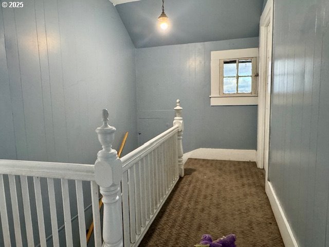 hallway with lofted ceiling, wooden walls, and dark colored carpet