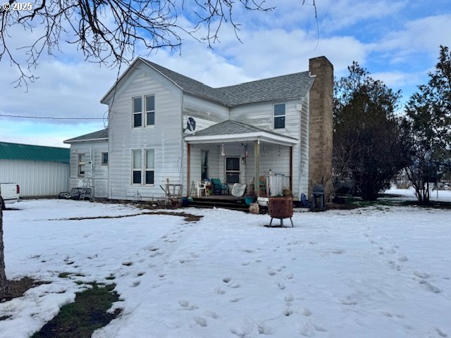 snow covered property featuring a porch and a chimney