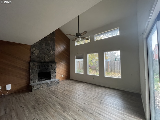 unfurnished living room with ceiling fan, a fireplace, wooden walls, light wood-type flooring, and high vaulted ceiling