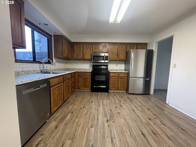 kitchen featuring appliances with stainless steel finishes, tasteful backsplash, light stone countertops, light hardwood / wood-style flooring, and sink