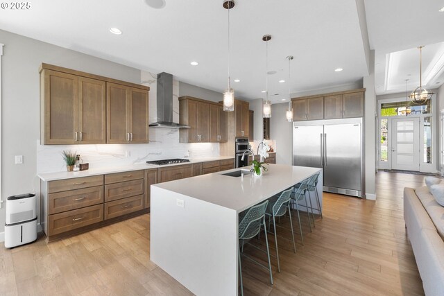 kitchen featuring wall chimney range hood, appliances with stainless steel finishes, decorative backsplash, and light wood-type flooring
