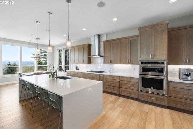 kitchen featuring wall chimney range hood, a kitchen breakfast bar, light countertops, a sink, and double oven