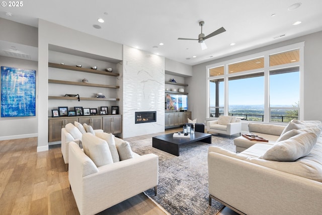 living area with ceiling fan, built in shelves, light wood-style flooring, and a fireplace