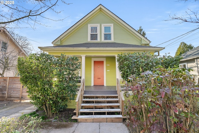 view of front of home featuring a porch, a shingled roof, and fence