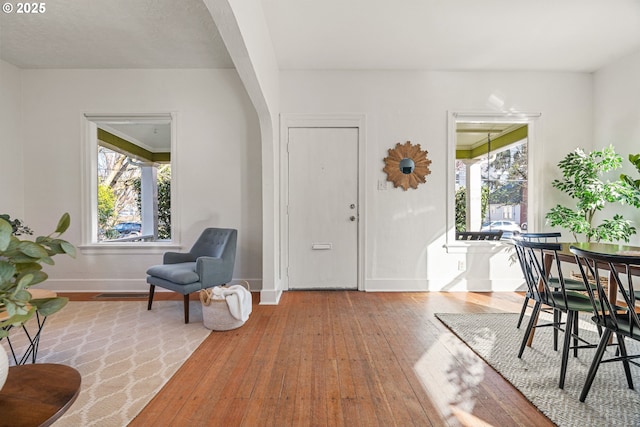 entryway with arched walkways, wood-type flooring, and baseboards