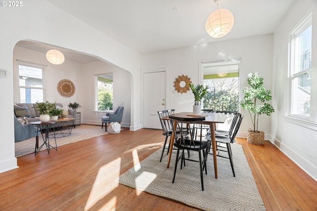 dining area with light wood finished floors, baseboards, and arched walkways