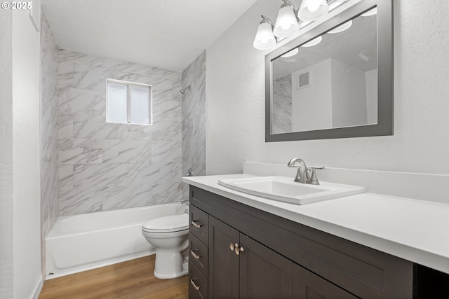 bathroom with a textured wall, toilet, vanity, wood finished floors, and  shower combination