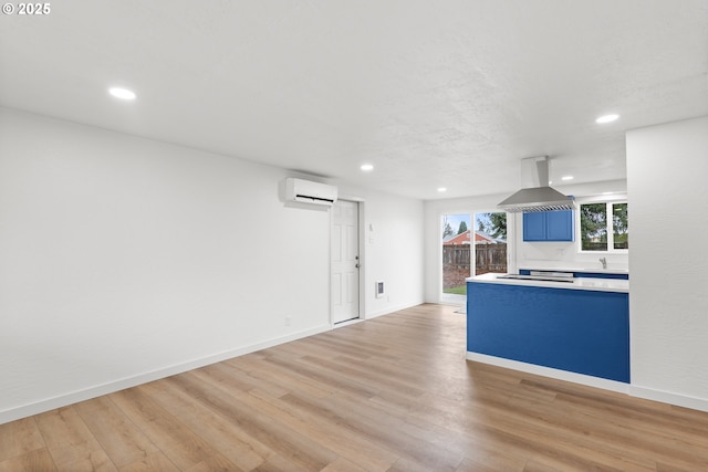 interior space with island range hood, baseboards, light countertops, light wood finished floors, and a wall mounted air conditioner