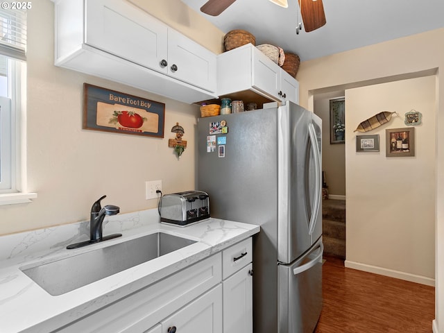 kitchen featuring freestanding refrigerator, a sink, a ceiling fan, and white cabinetry