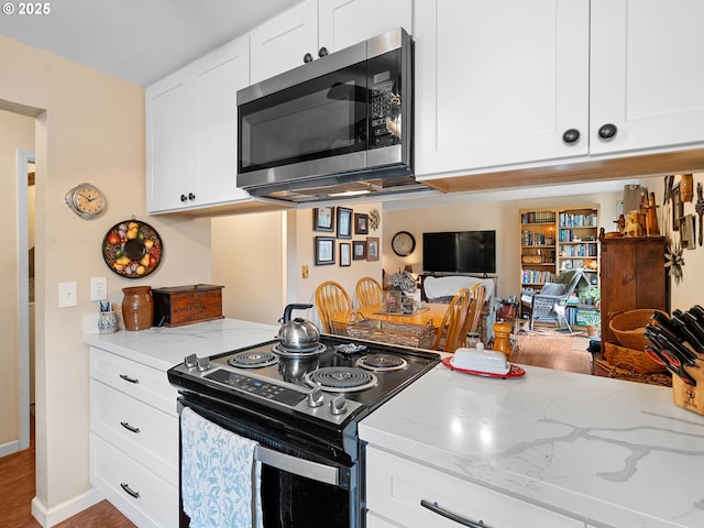 kitchen with range with electric cooktop, stainless steel microwave, light stone countertops, and white cabinetry