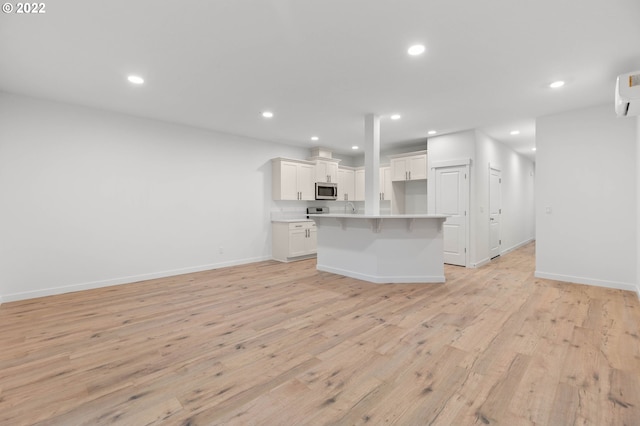 kitchen featuring light wood-type flooring, baseboards, white cabinets, stainless steel microwave, and open floor plan