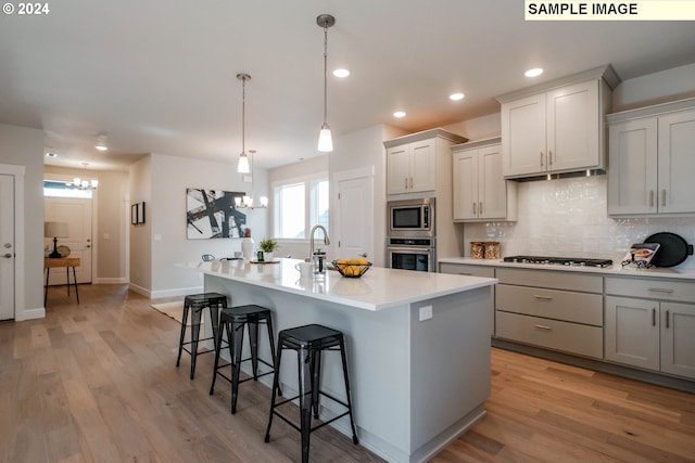 kitchen with backsplash, a kitchen bar, appliances with stainless steel finishes, light countertops, and an inviting chandelier