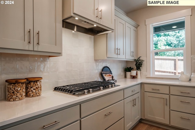 kitchen with light countertops, stainless steel gas cooktop, under cabinet range hood, and backsplash