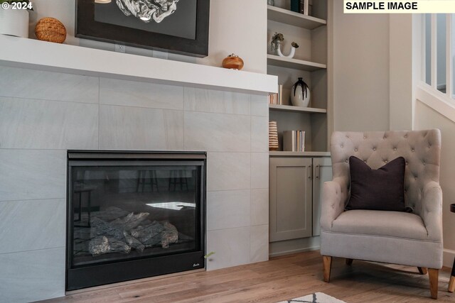 sitting room featuring built in shelves, light wood-type flooring, and a tile fireplace