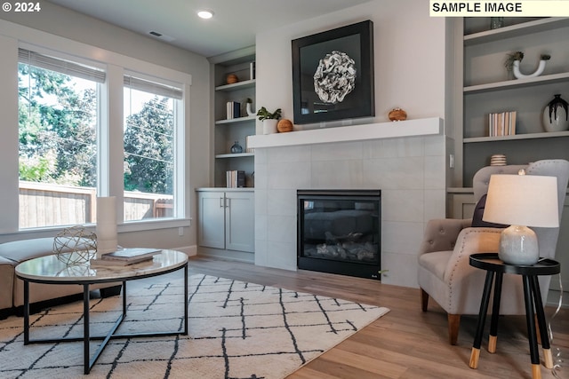 sitting room with visible vents, a tiled fireplace, built in features, wood finished floors, and baseboards