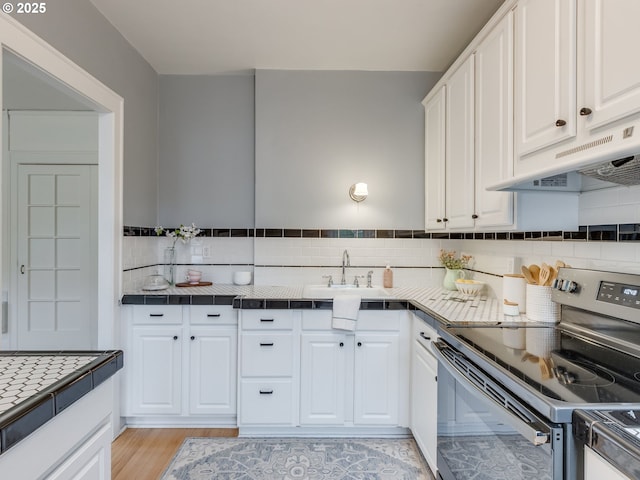 2015 NW Flanders St Unit 511, Portland, OR 97209 - kitchen featuring stainless steel range with electric stovetop, tile countertops, white cabinetry, backsplash, and under cabinet range hood