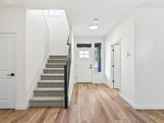foyer entrance featuring baseboards, stairs, and light wood finished floors