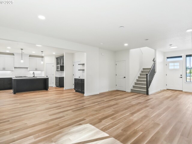 unfurnished living room with recessed lighting, a sink, light wood-style flooring, and stairs