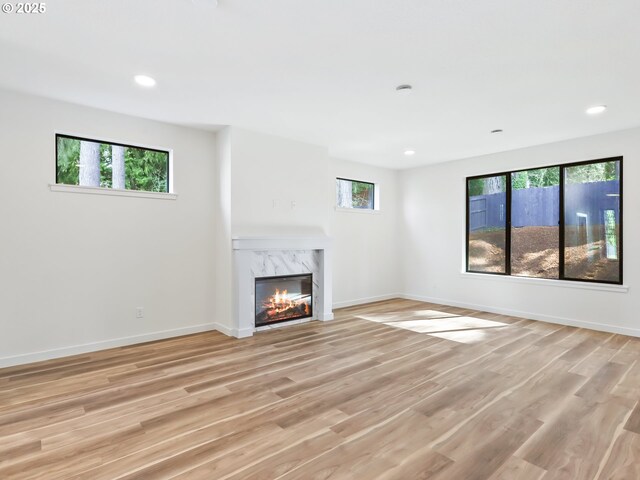 unfurnished living room with plenty of natural light, light wood finished floors, and a high end fireplace