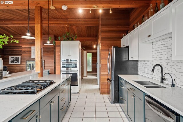 kitchen with decorative backsplash, appliances with stainless steel finishes, wood ceiling, a sink, and wooden walls